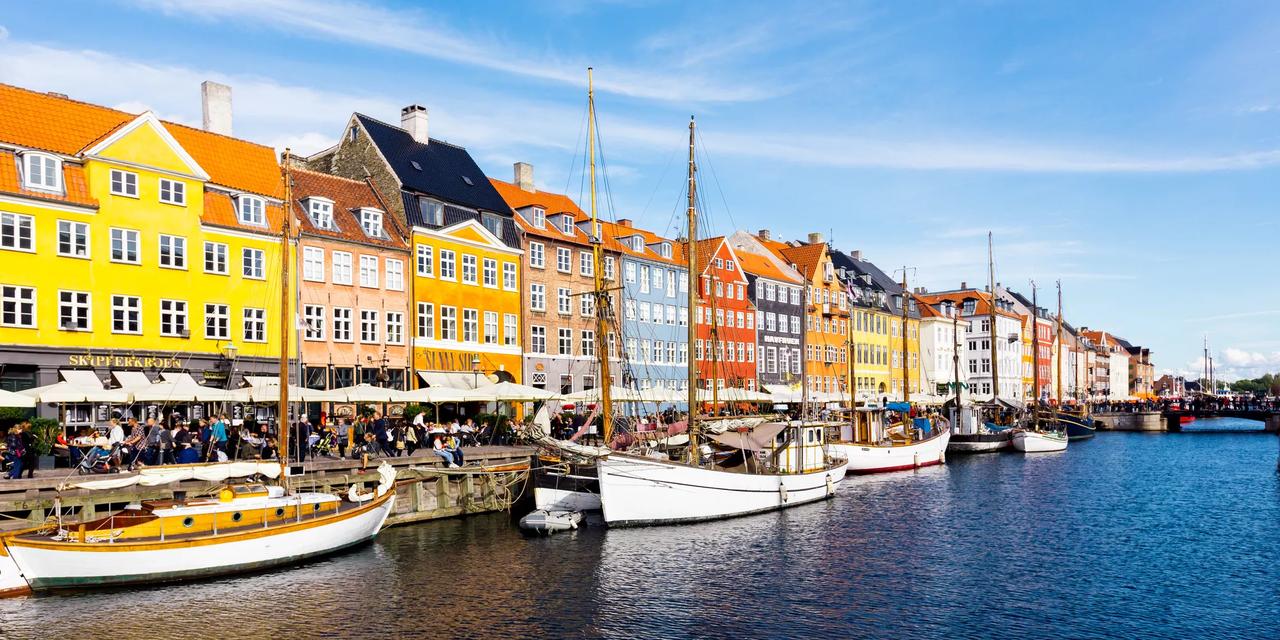 Nyhavn i K&oslash;benhavn en solrik dag, med fargerike byg&aring;rder, uteserveringer og gamle seilb&aring;ter langs kanalen
