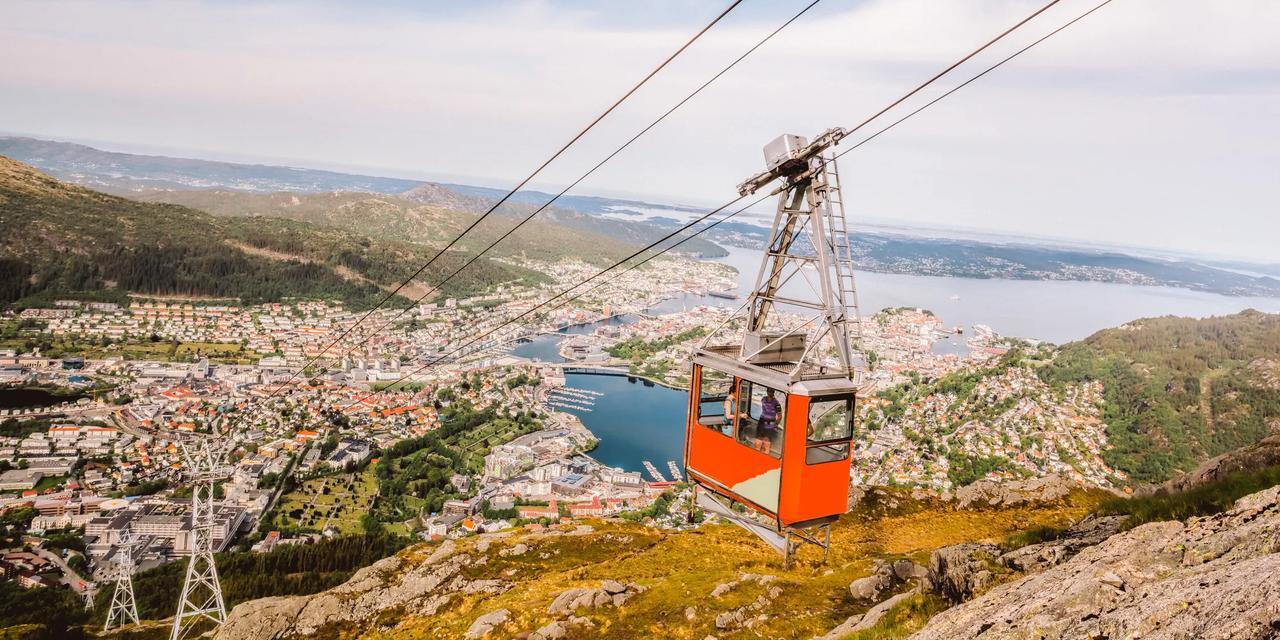 Den r&oslash;de gondolen til Ulriksbanen p&aring; vei opp Ulriken, med utsikt over Bergen sentrum, Store Lungeg&aring;rdsvann og fjorden.