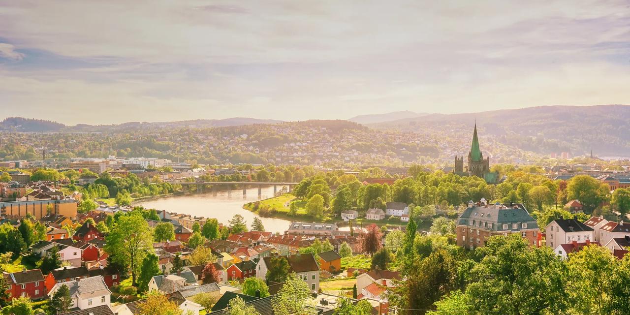 Utsikt over Trondheim med Nidelva, Gamle Bybro og Nidarosdomen omgitt av gr&oslash;nne tr&aelig;r.